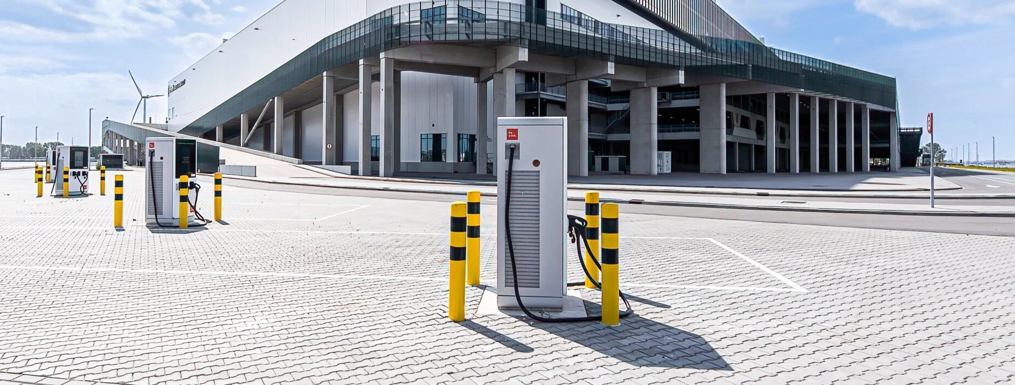 Leeg parkeerterrein met elektrische laadpalen van Floading voor voertuigen, voor het moderne glazen gebouw van CTPark Amsterdam City