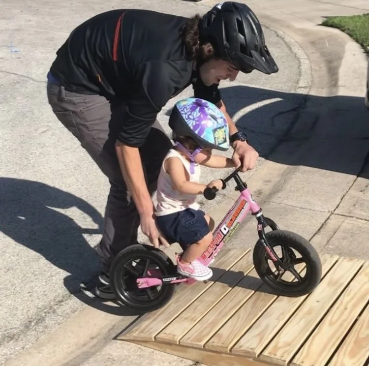 Coach Andrew Garza helping a toddler ride a pink balance bike