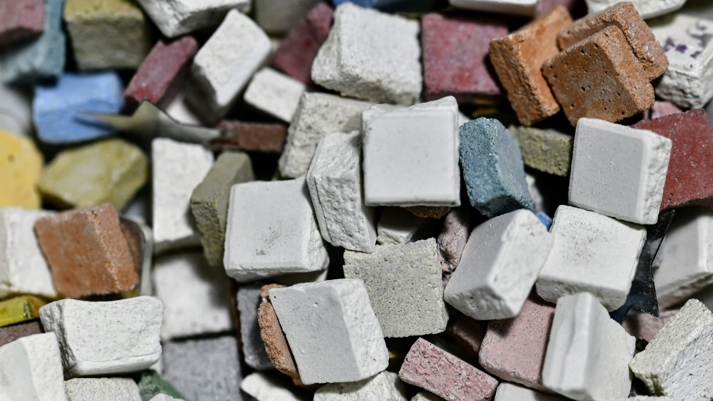 Close-up of a pile of small, colorful, rectangular and square mosaic tiles made of various materials such as ceramic and stone.