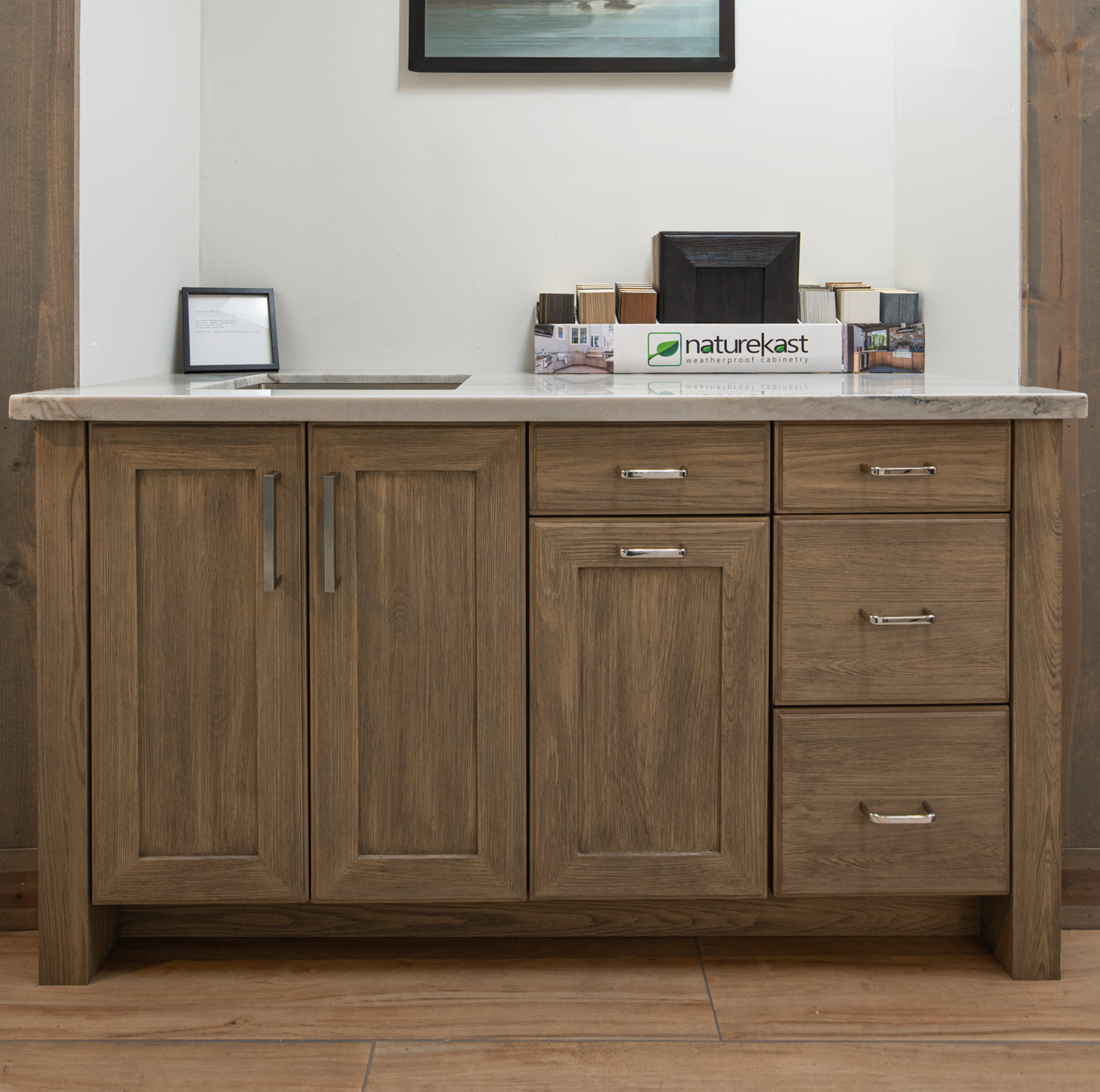 A wooden cabinet with a white countertop, holding sample materials and a box labeled 'naturekast weatherproof cabinetry'.