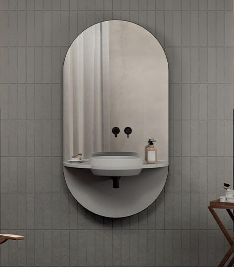 A modern bathroom mirror with a built-in sink, mounted on a tiled wall, with a soap dispenser and small decorative items on the shelf.