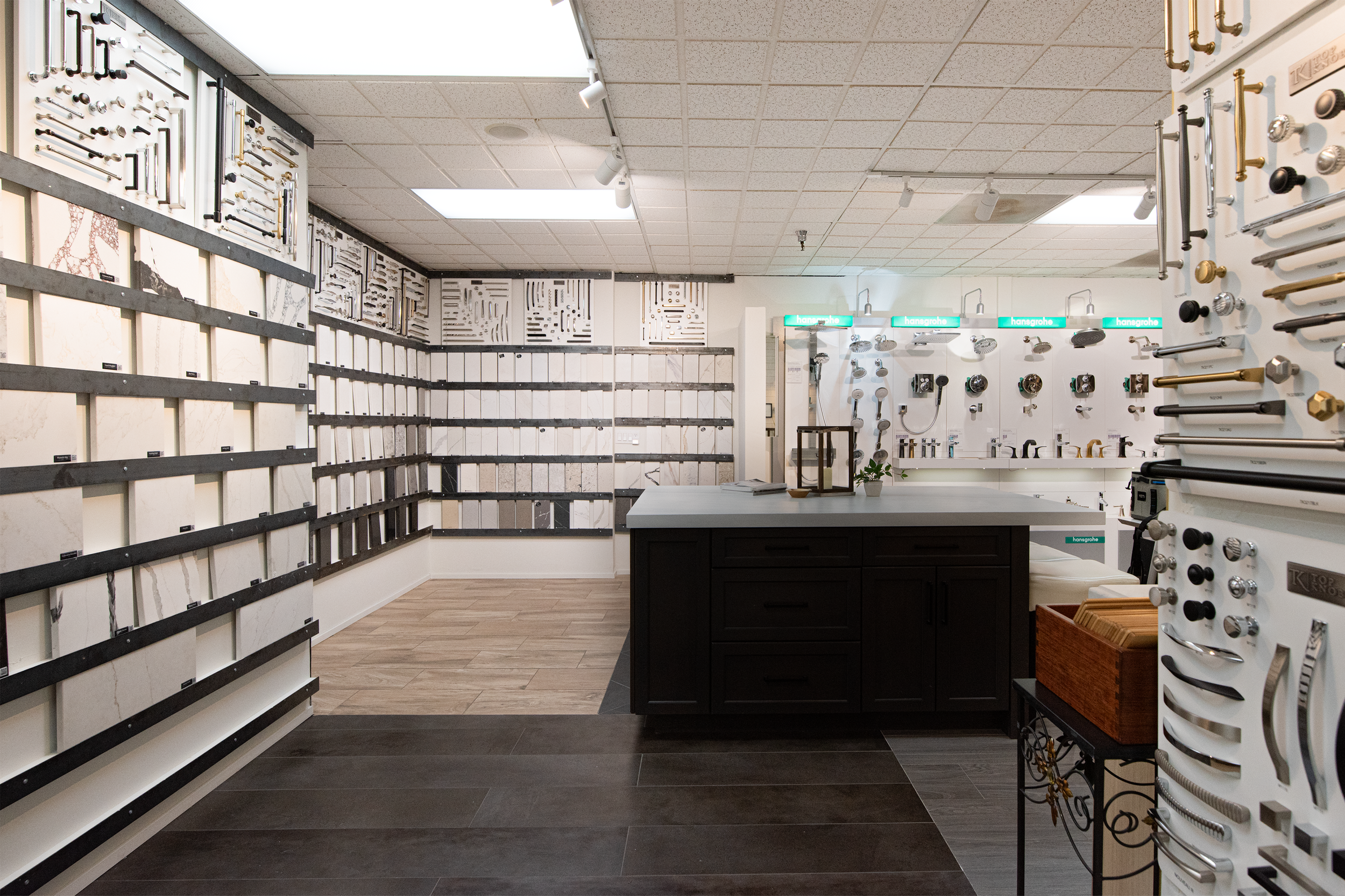 Showroom with various bathroom fixtures and fittings, including showerheads, faucets, and handles displayed on walls and shelves, with a central island and a dark wood cabinet.