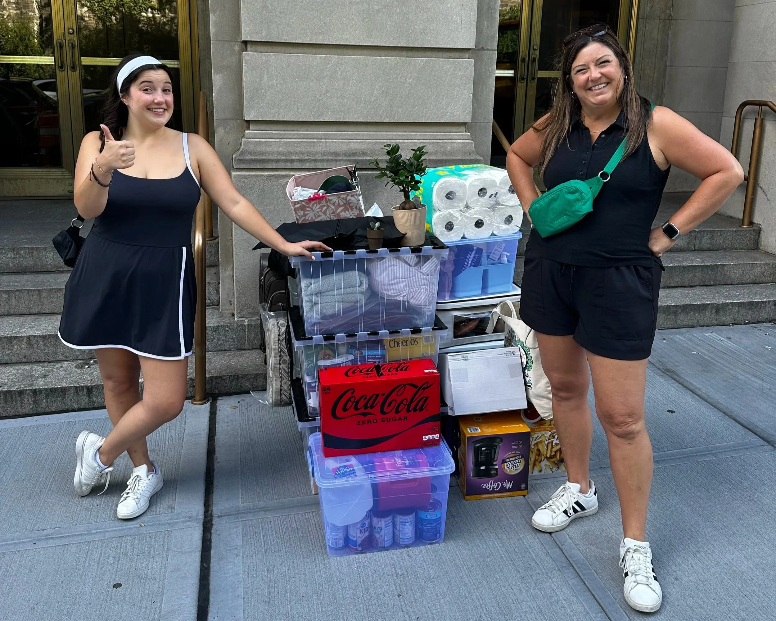 Liz and her daughter Isabel stand beside a cart overflowing with college move-in supplies, highlighting the excitement and expense of preparing for a new school year.