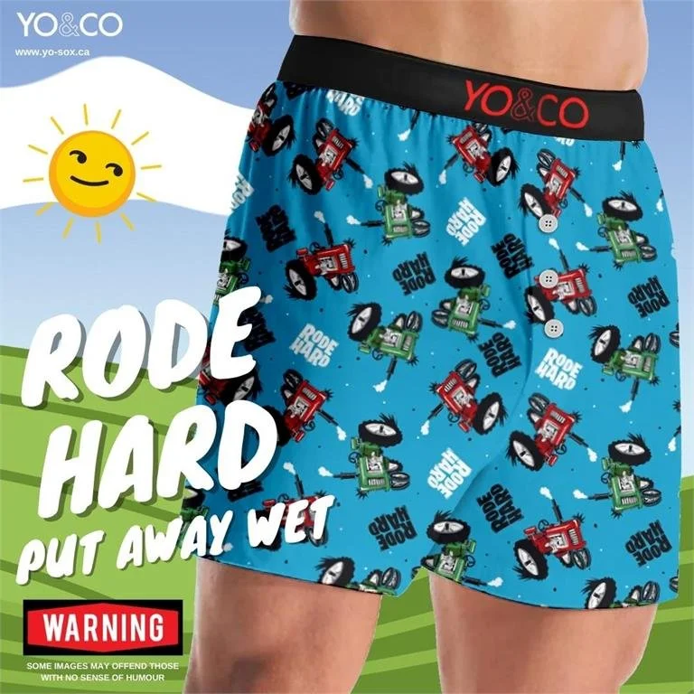 Men's boxer shorts featuring a colorful pattern of cartoon flashlights and the text 'DOPE HARD'. The shorts have a black waistband with red and white text 'YO & CO'. The background is a cartoonish weather scene with a smiling sun and green hills, with bold text on the left side saying "RODE HARD PUT AWAY WET" and a red warning label at the bottom.