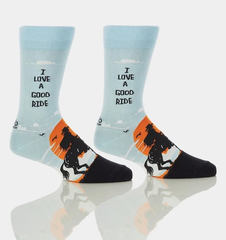 Pair of socks with a dinosaur design, light blue background, and the phrase 'I love a good ride'