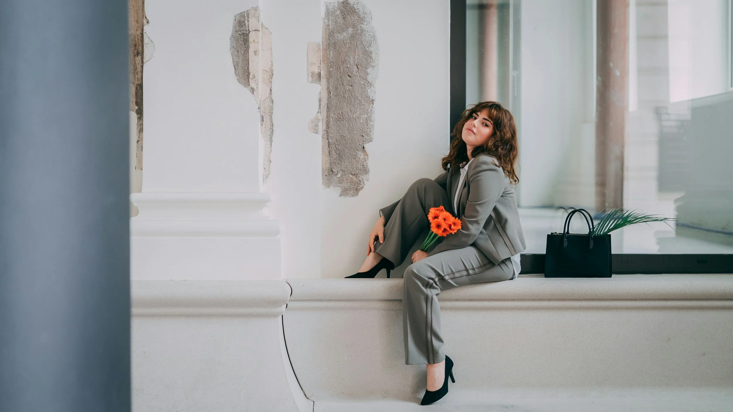 business woman sits on wall of NYC building. has orange flowers in her hand.