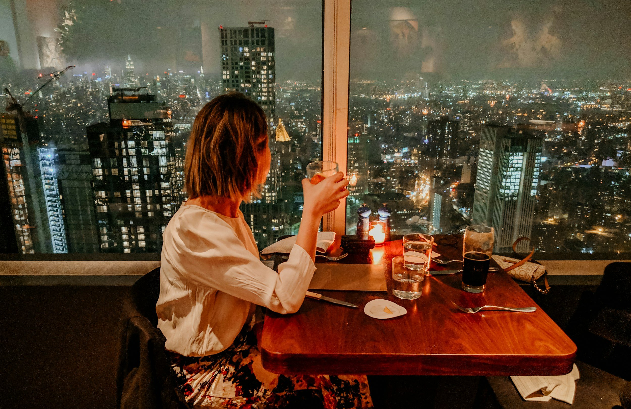 woman sits with mocktail in hand looking out window overlooking NYC