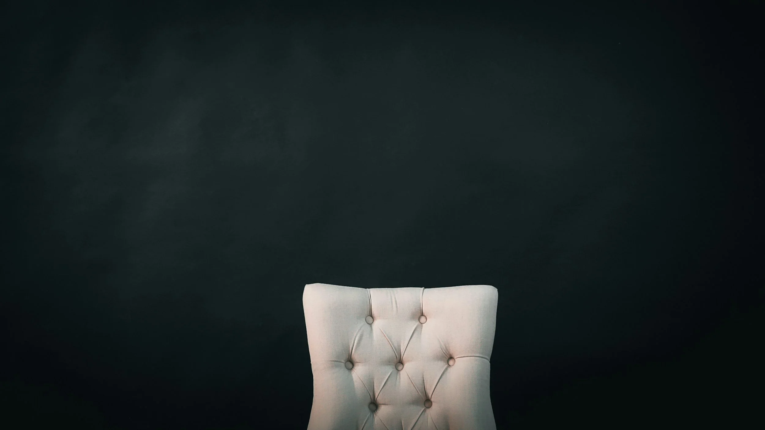beige chair is placed in front of a black wall