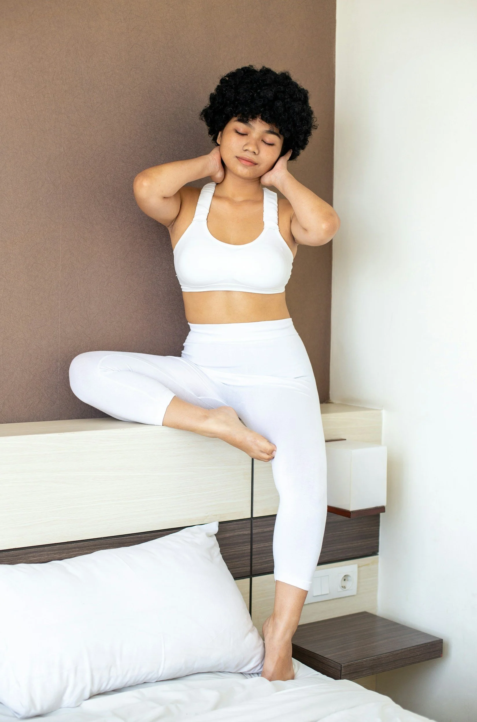 Person in workout clothes sitting on bed at home.