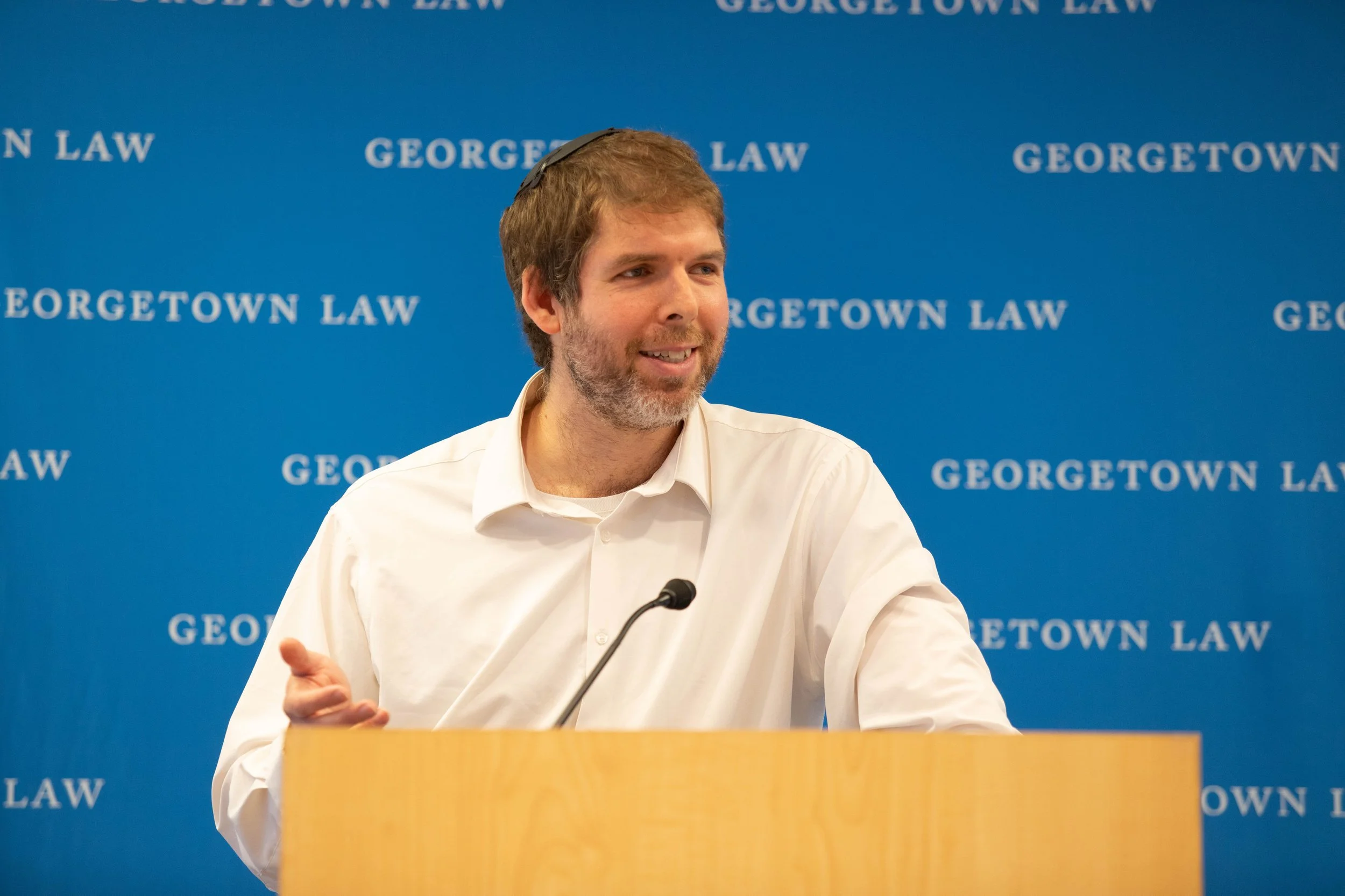 Unplug Author Richard Simon at a podium in front of a blue backdrop with white text that reads 'Georgetown Law'.