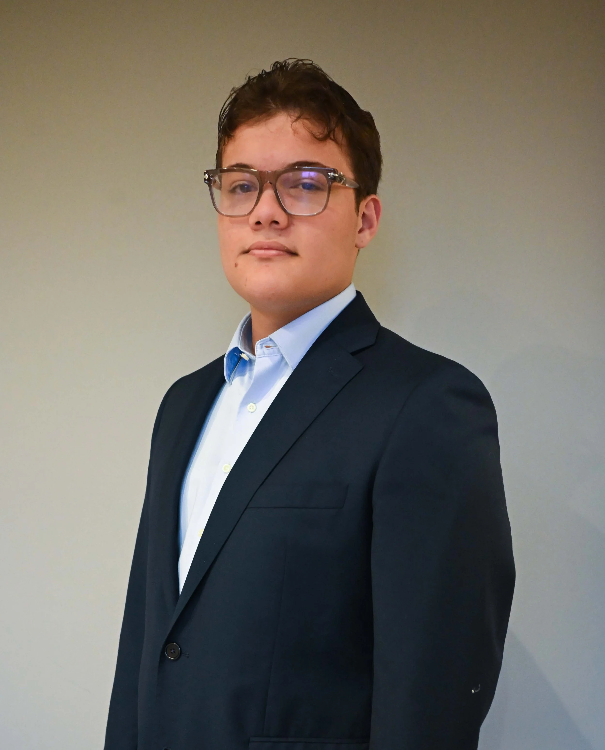 Young man in a suit standing in front of a geometric patterned wall.