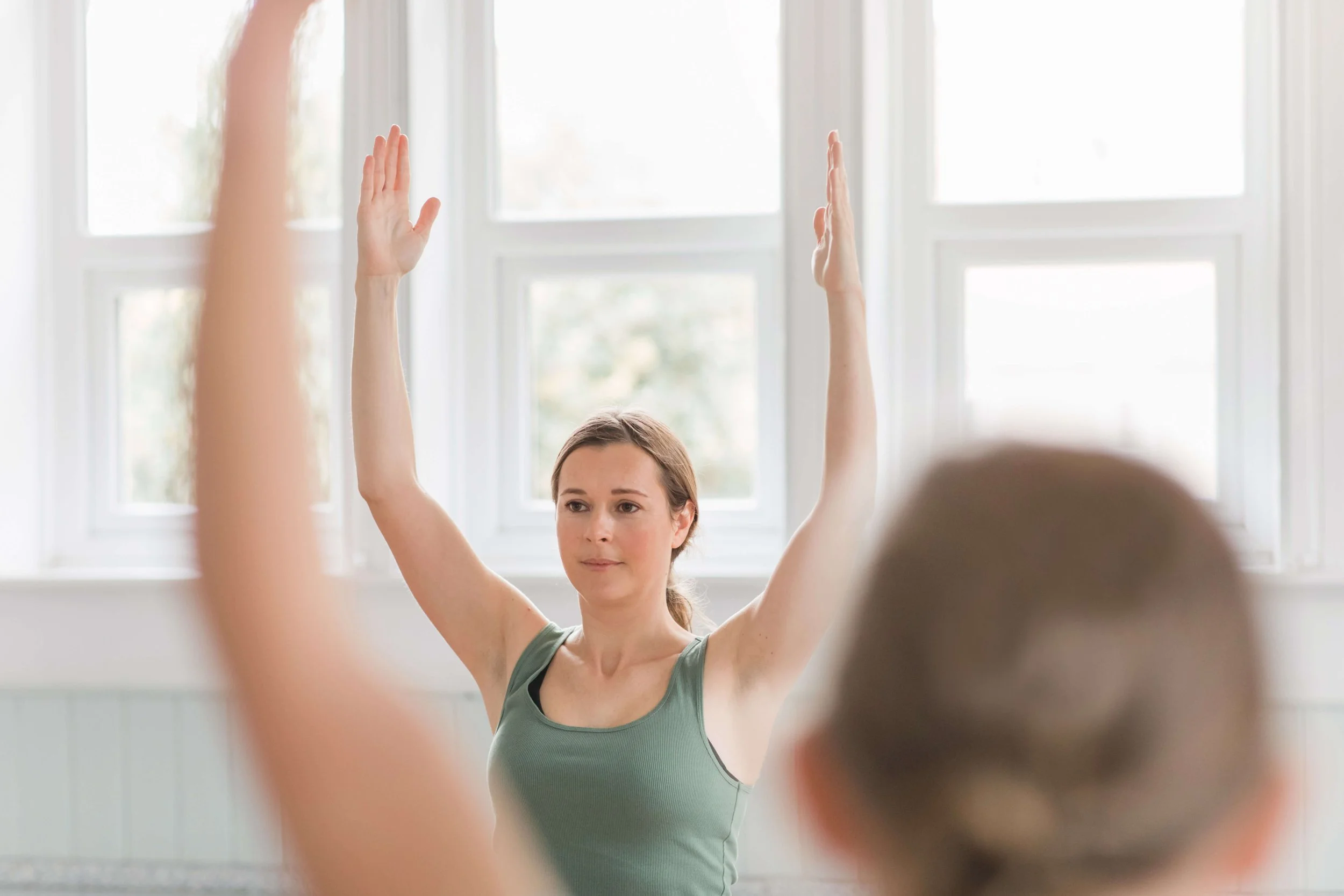 Jess Evans from Jess Evans Yoga teaches a welcoming beginners yoga class in Easingwold. She stands with arms raised at the front of the class.