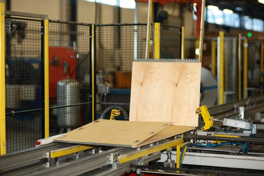Automated woodworking machine processing a wooden panel in a factory setting.