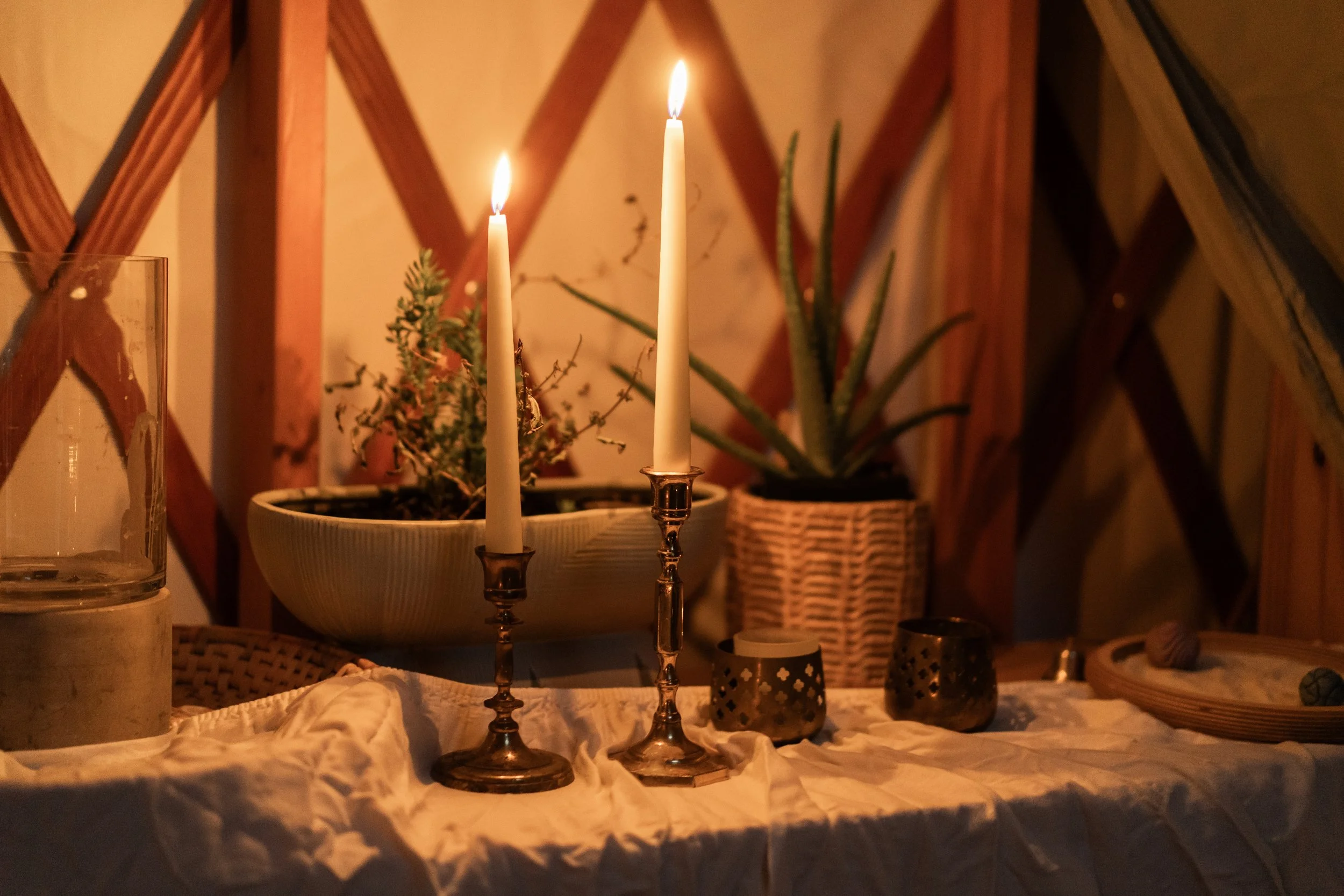 Candles on a table with potted plants, candles, and decorative items, illuminated in warm light.