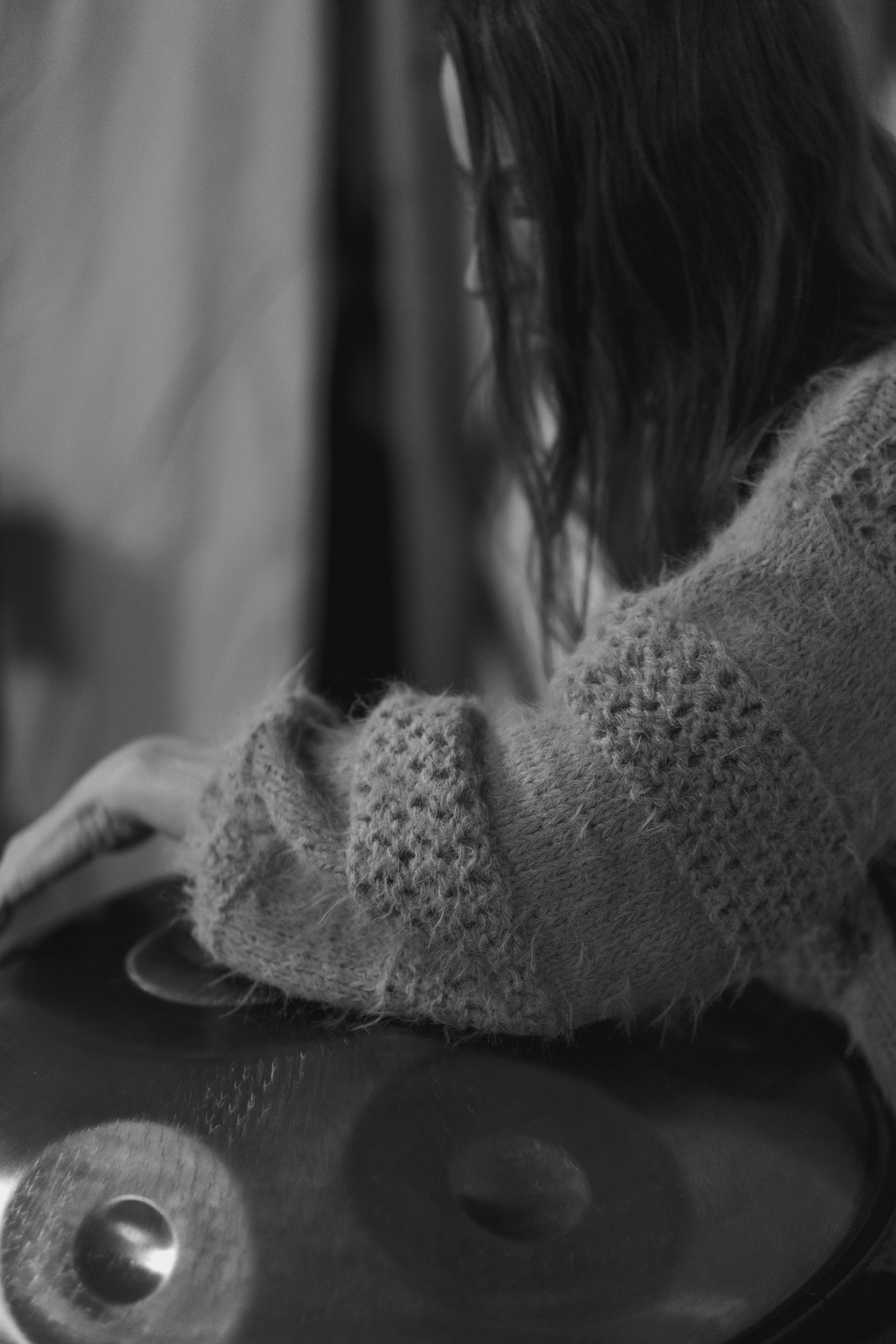 A woman with long hair wearing a cozy, knitted sweater leaning over a turntable, adjusting the record.