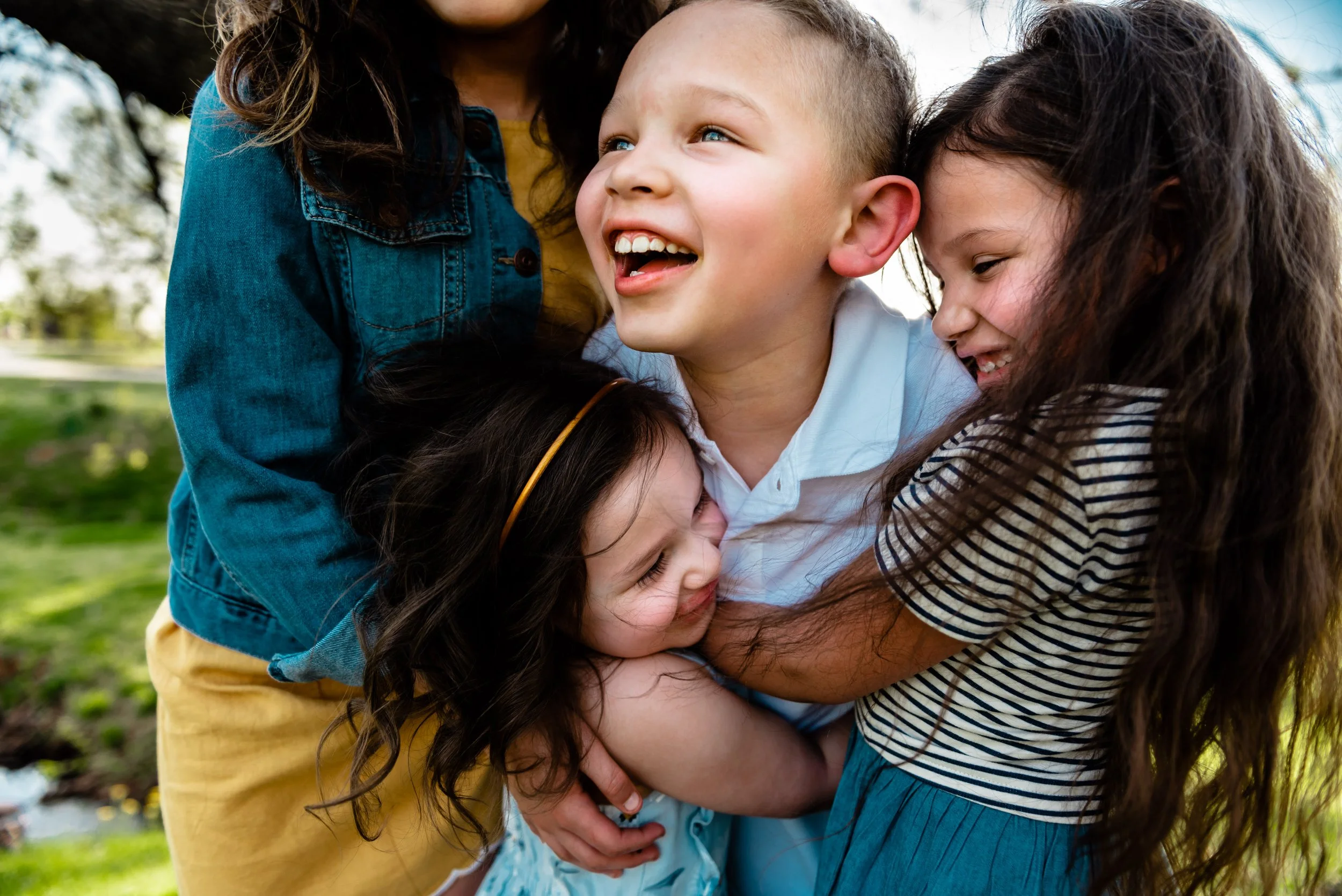 Four children hugging and smiling outdoors in a park.