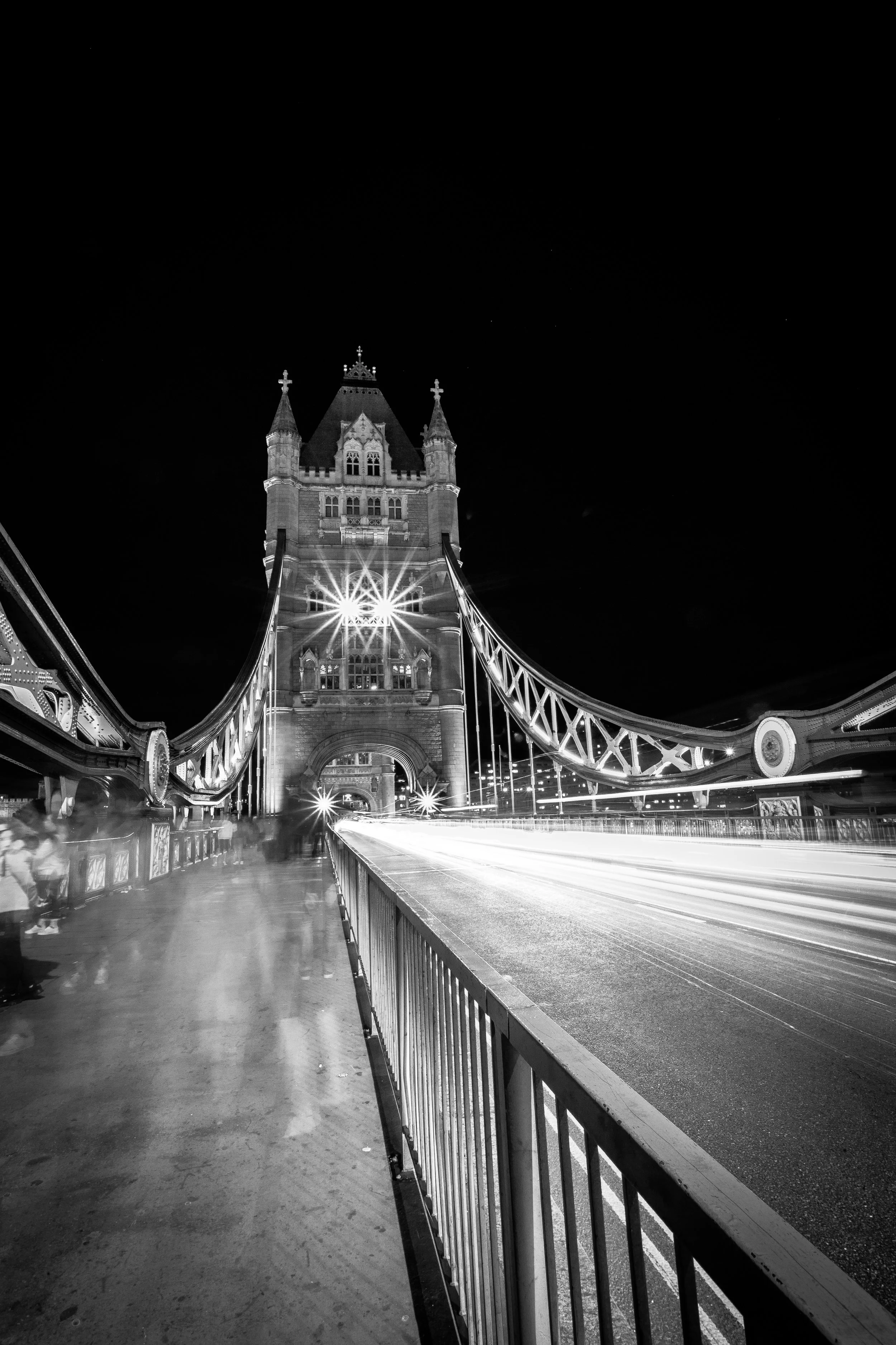 Nighttime black and white photo of Tower Bridge in London, with blurred cars creating light trails on the bridge.