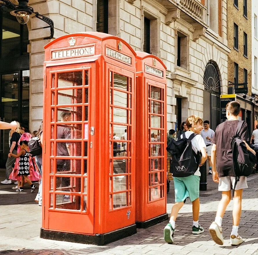 Red British-style telephone booth on a busy city street, with people walking nearby.