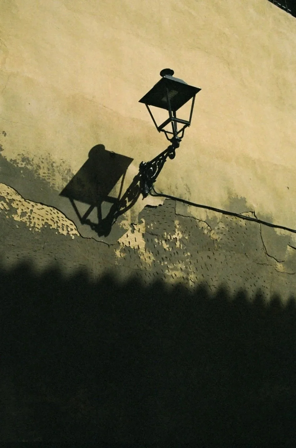 Street lamp casting a shadow on a yellow wall with peeling paint, at night.