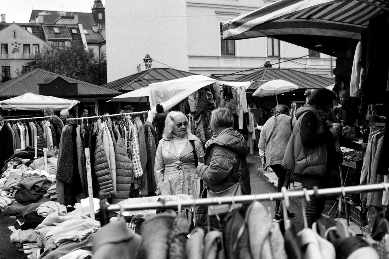 People shopping at an outdoor market with clothing racks and tables selling various items.