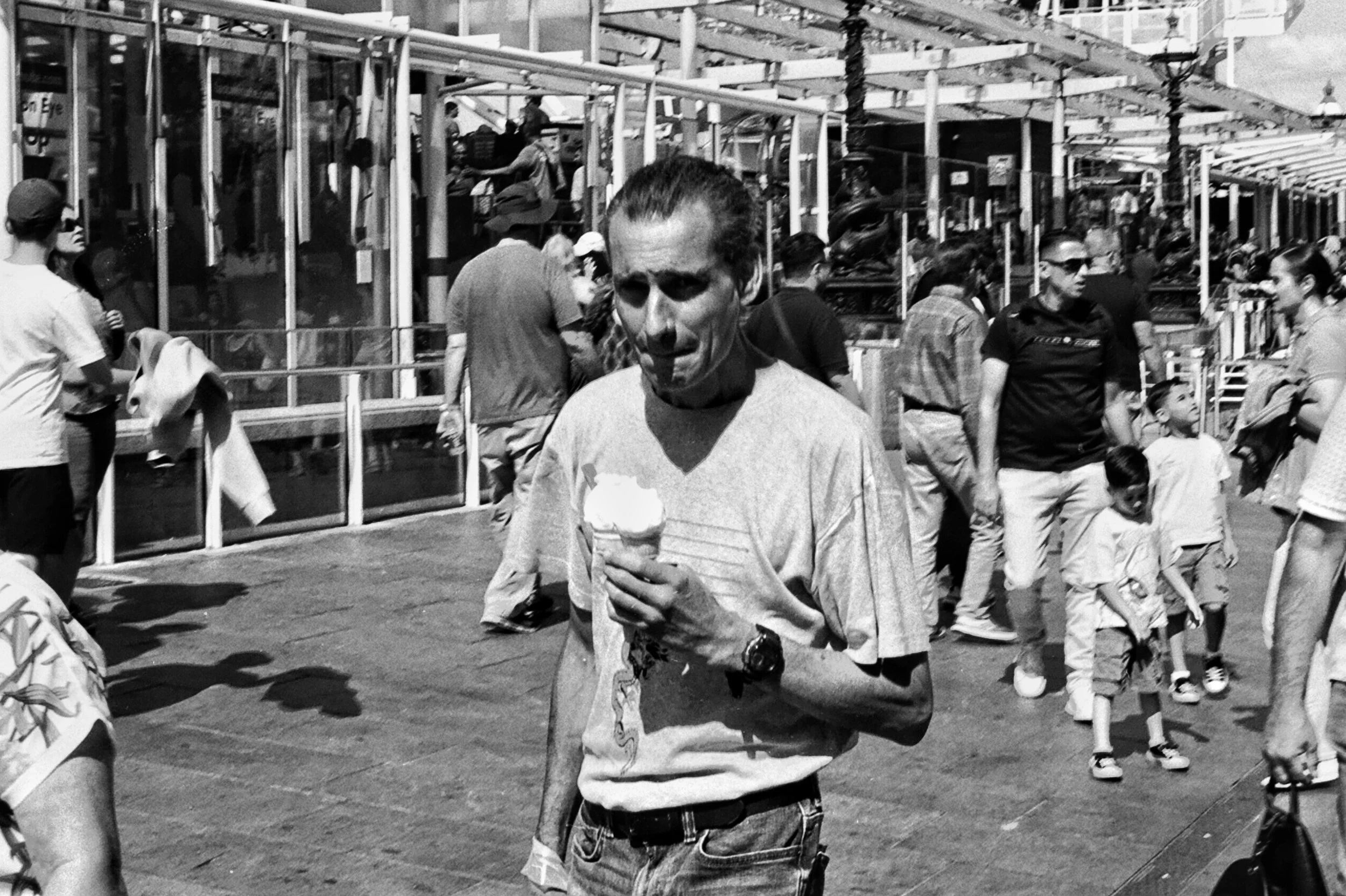 A man holding an ice cream cone in a crowded outdoor area, with various people walking and interacting around him.