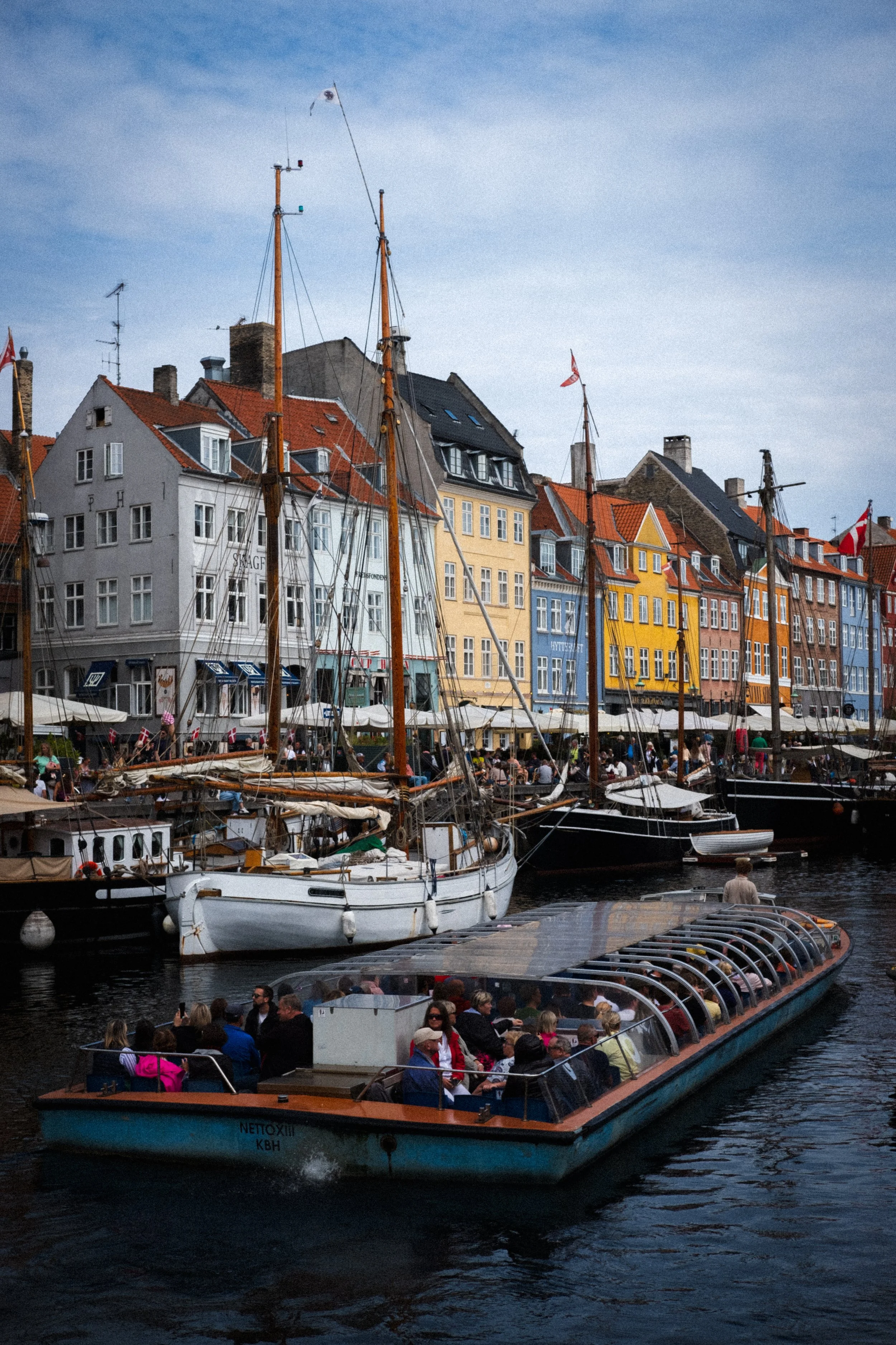 Colorful buildings lining a waterfront with boats and a glass-covered sightseeing boat filled with tourists.