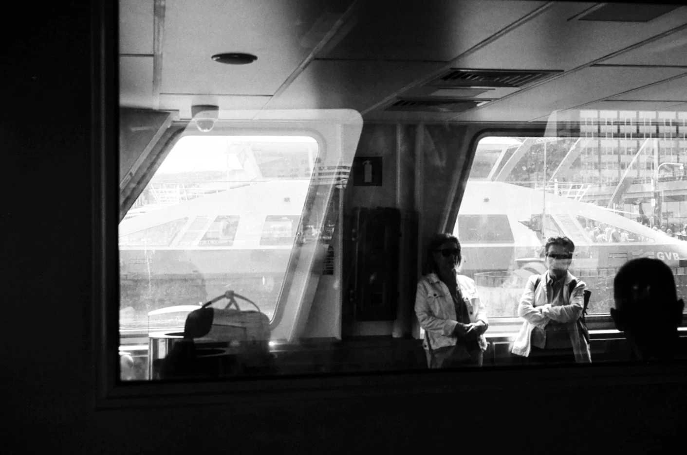 Black and white photo of three people standing inside an airport terminal near windows, with airplanes visible outside.