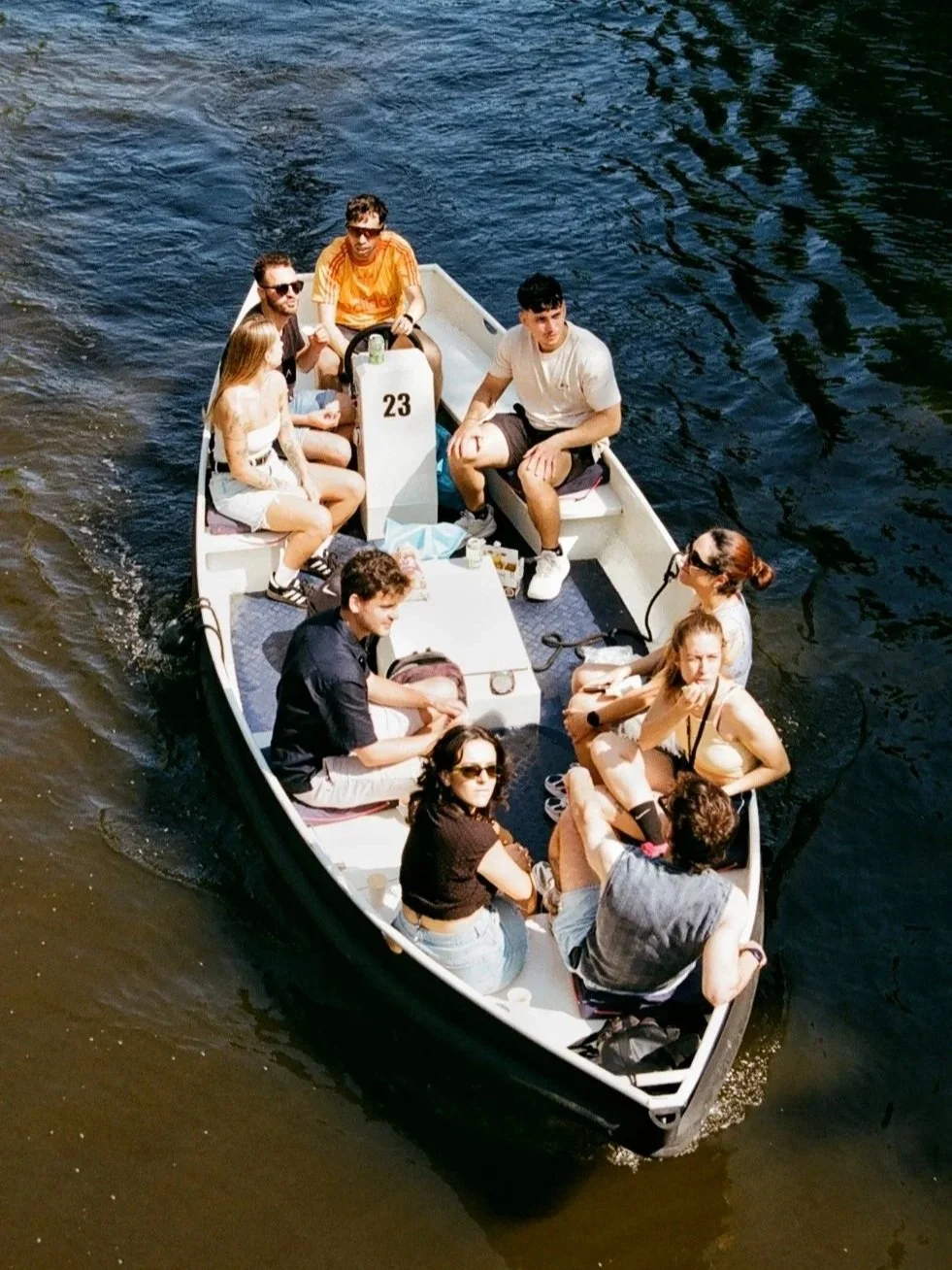 A group of nine people sitting on a boat with a dark water background, some wearing sunglasses and casual clothes, enjoying a boat ride.