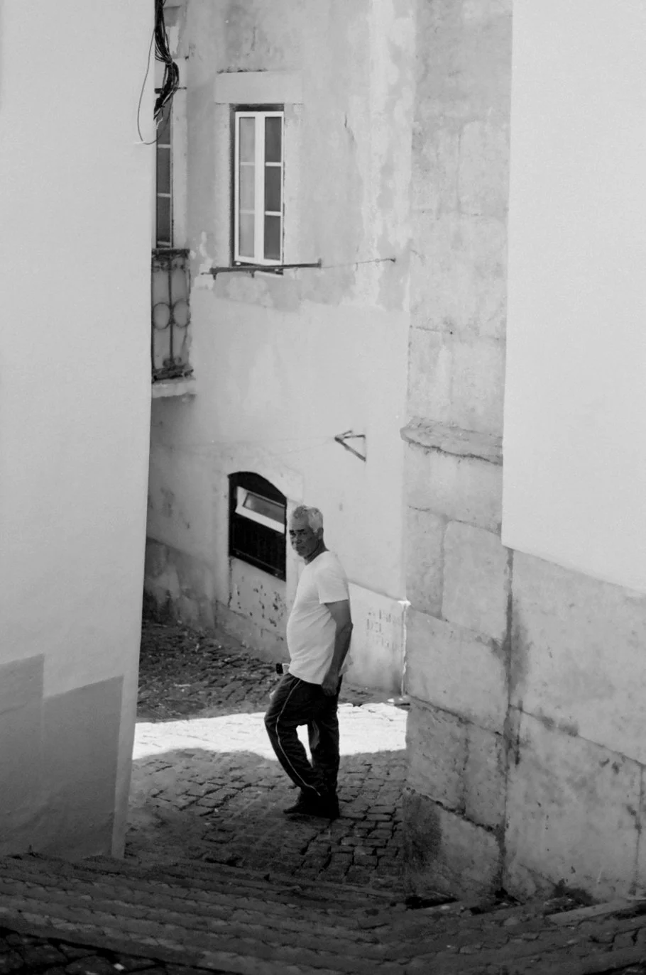 A man walking down a cobblestone street with old buildings on either side, in black and white.