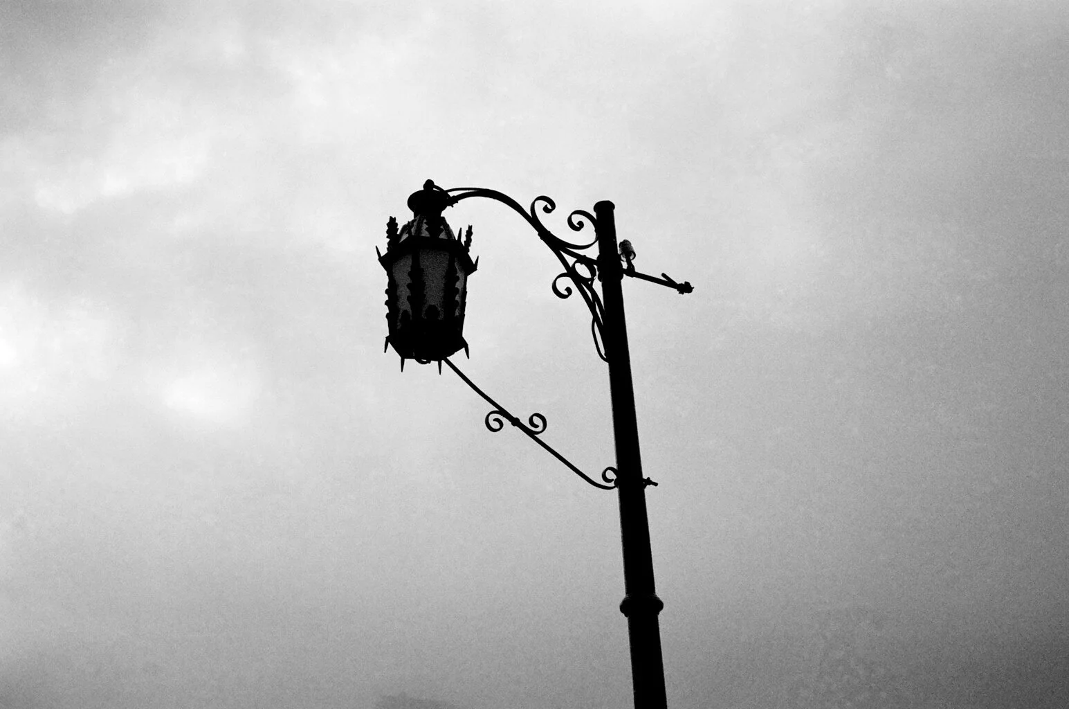 Black silhouette of a vintage street lamp against a cloudy sky.