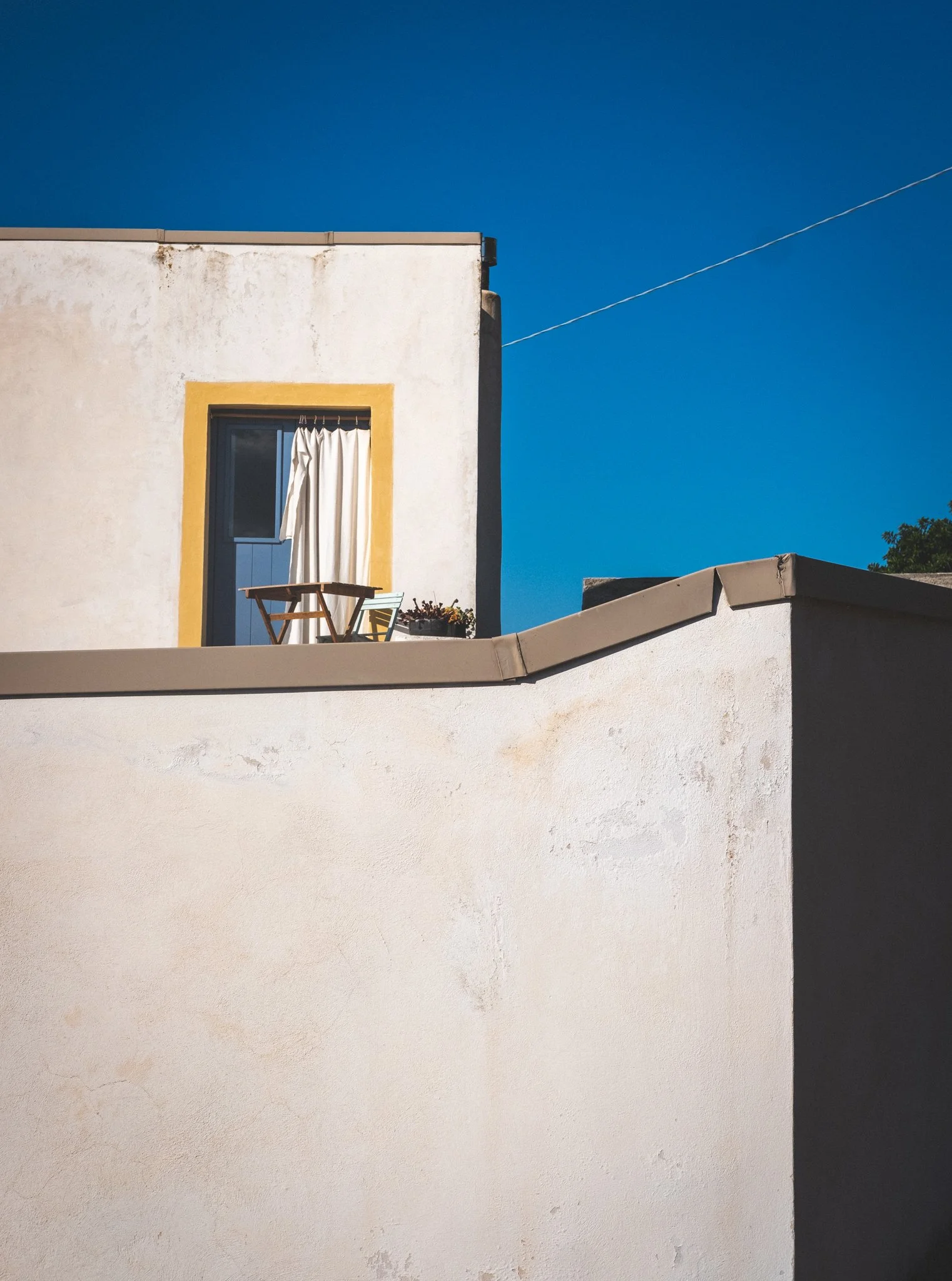 A white building with a small balcony and closed white curtains, against a clear blue sky.
