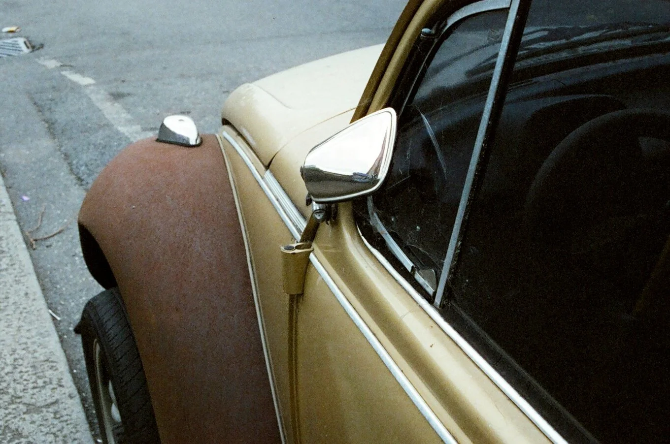 Close-up of a vintage car showing the side mirror, front fender, and part of the windshield, parked on the street.