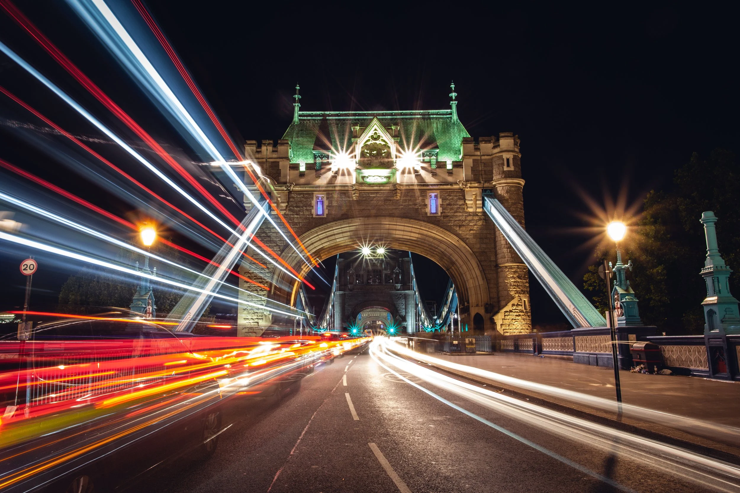Night view of Tower Bridge in London with light trails from moving vehicles.