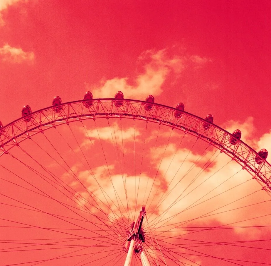 A large Ferris wheel against a pink sky with clouds.