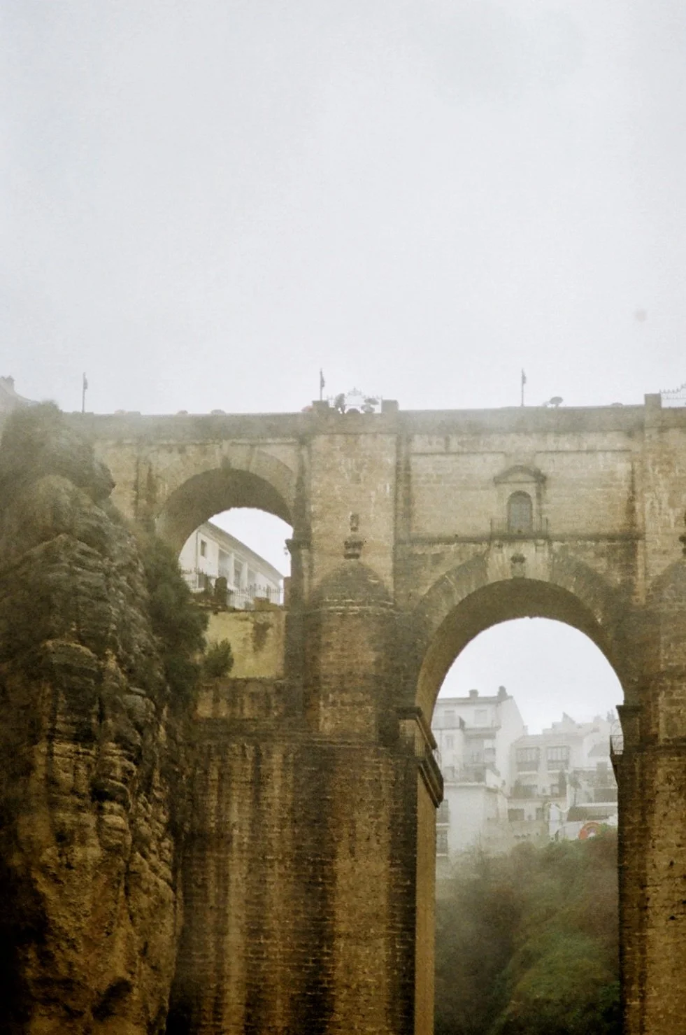 An old stone aqueduct with multiple arches crossing a deep canyon, with buildings visible in the background.