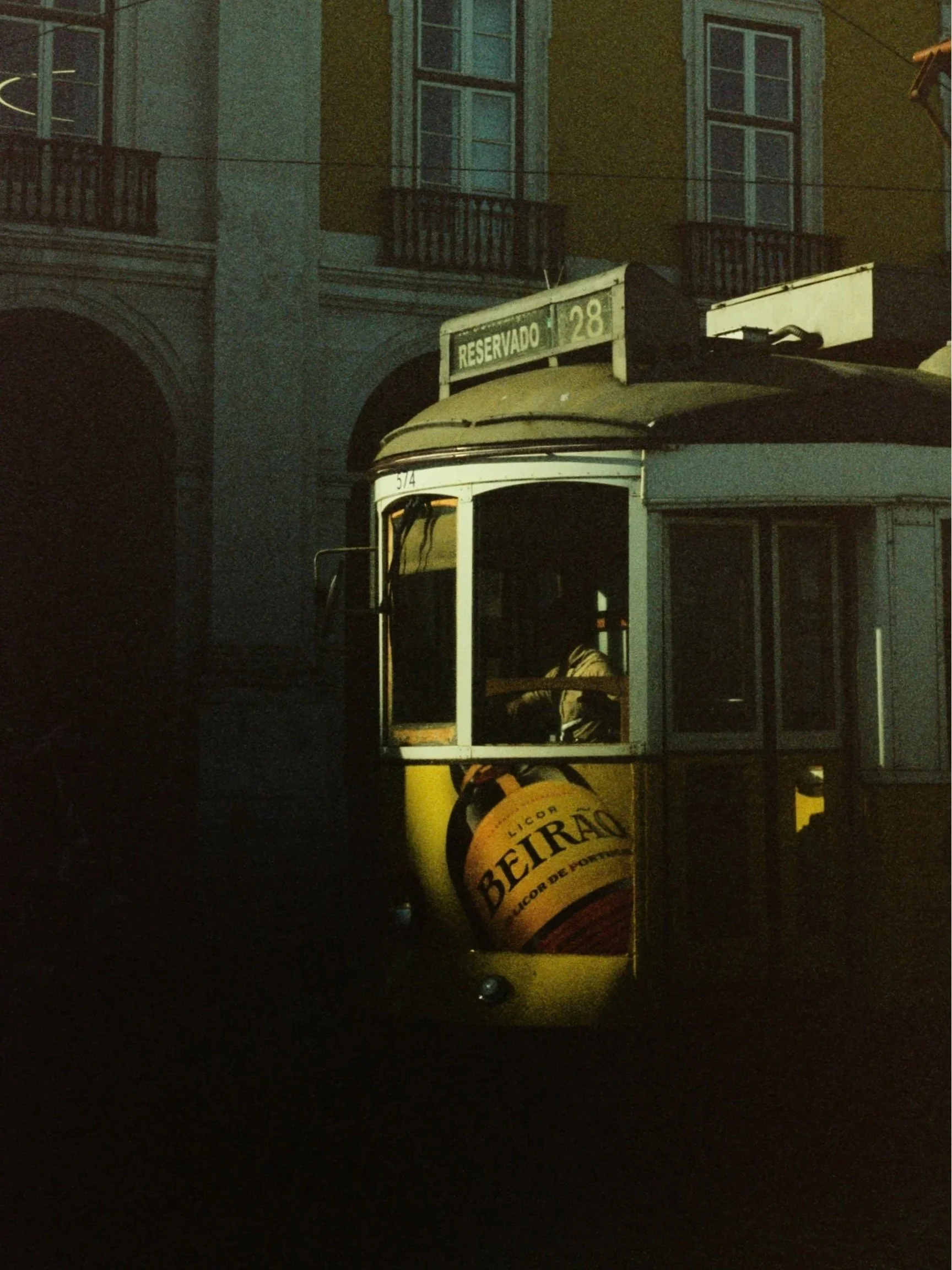 Vintage tram with a Beirao advertisement on the side, parked at night near old buildings with balconies.