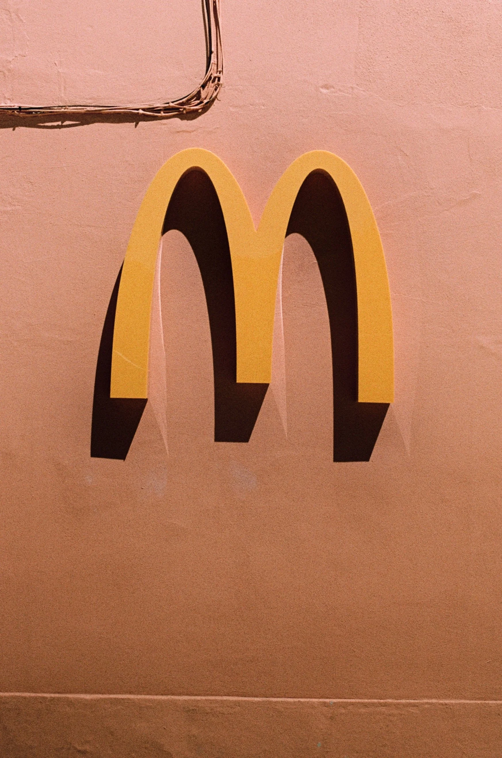 Close-up of a McDonald's logo with yellow arches on a pink wall.