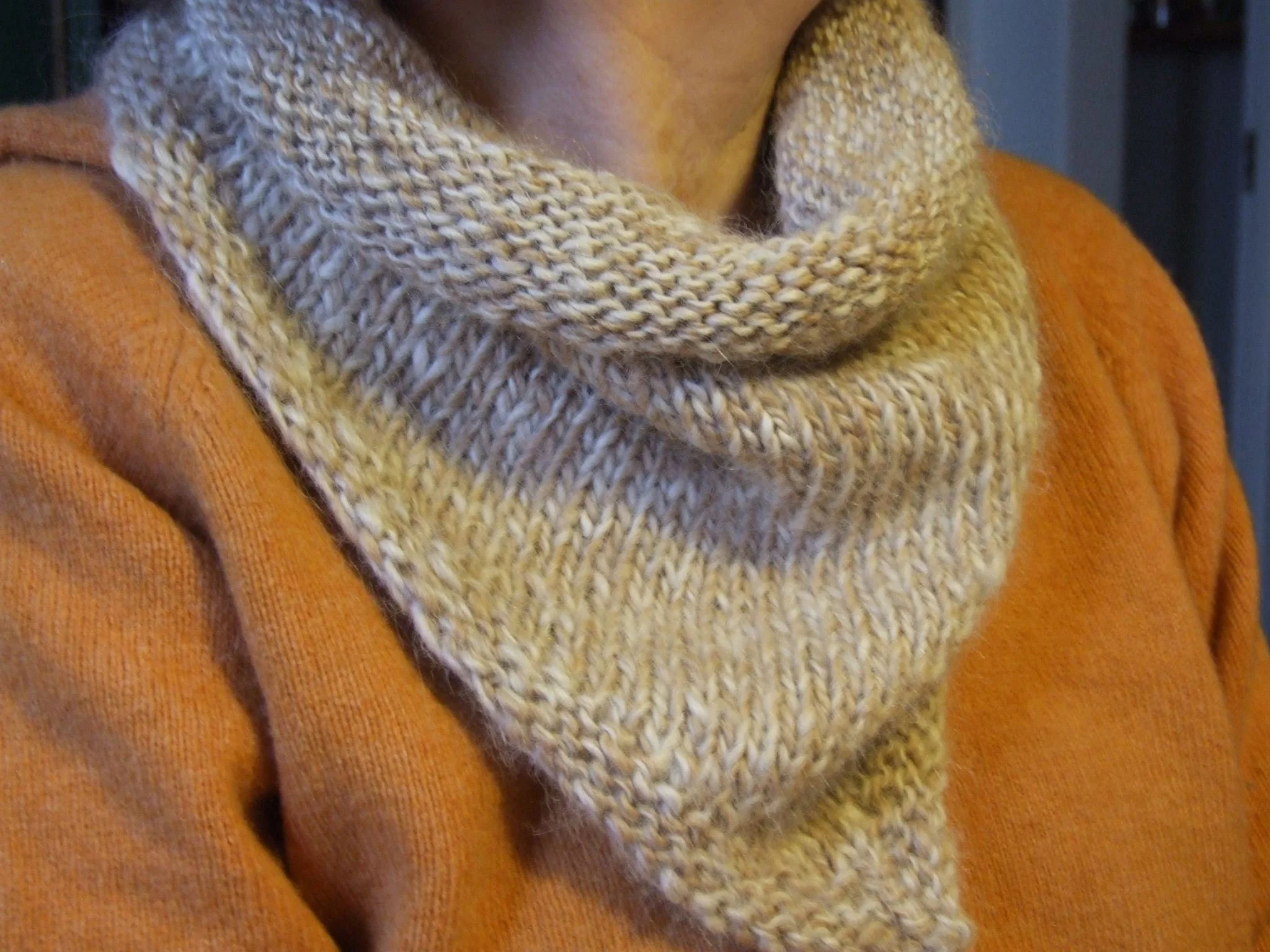 A close-up of a person wearing a beige knitted scarf and an orange sweater. Made at Monte Frio Alpacas. 