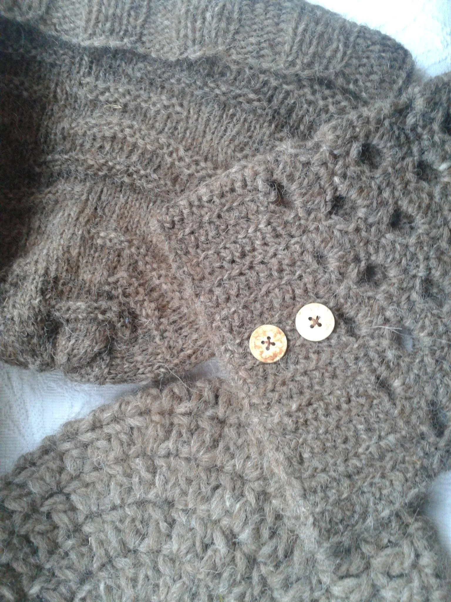 Close-up image of a thick, brown, knitted wool sweater with two wooden buttons near the bottom. Made at Monte Frio Alpacas. 