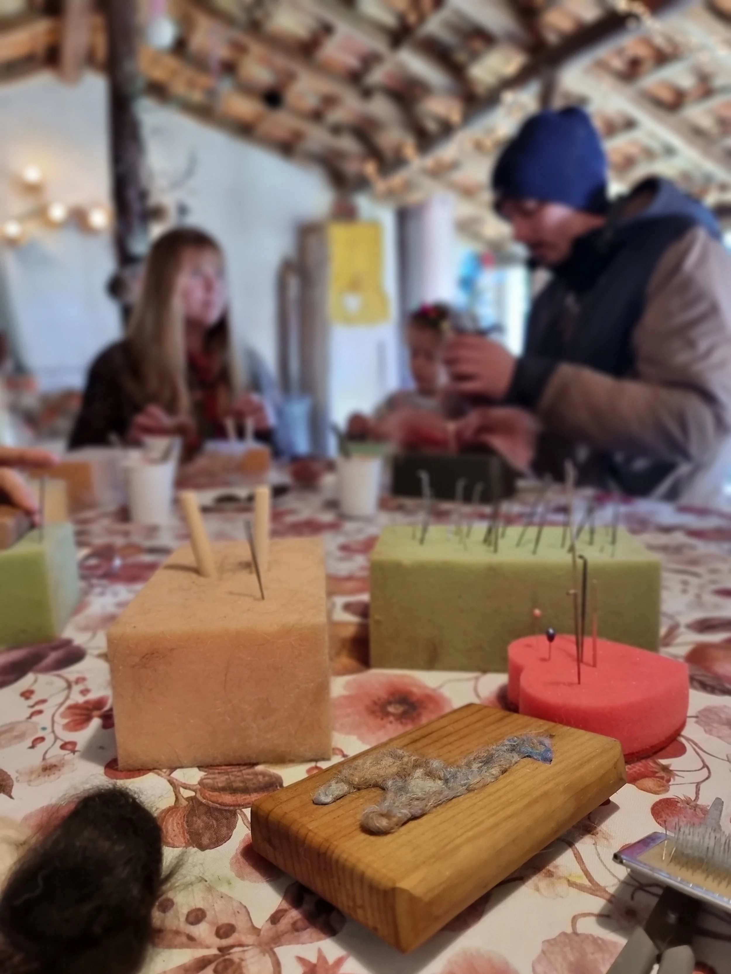 Close-up view of small animals and felted wool projects on a table at Monte Frio Alpacas, with blurred people in the background.