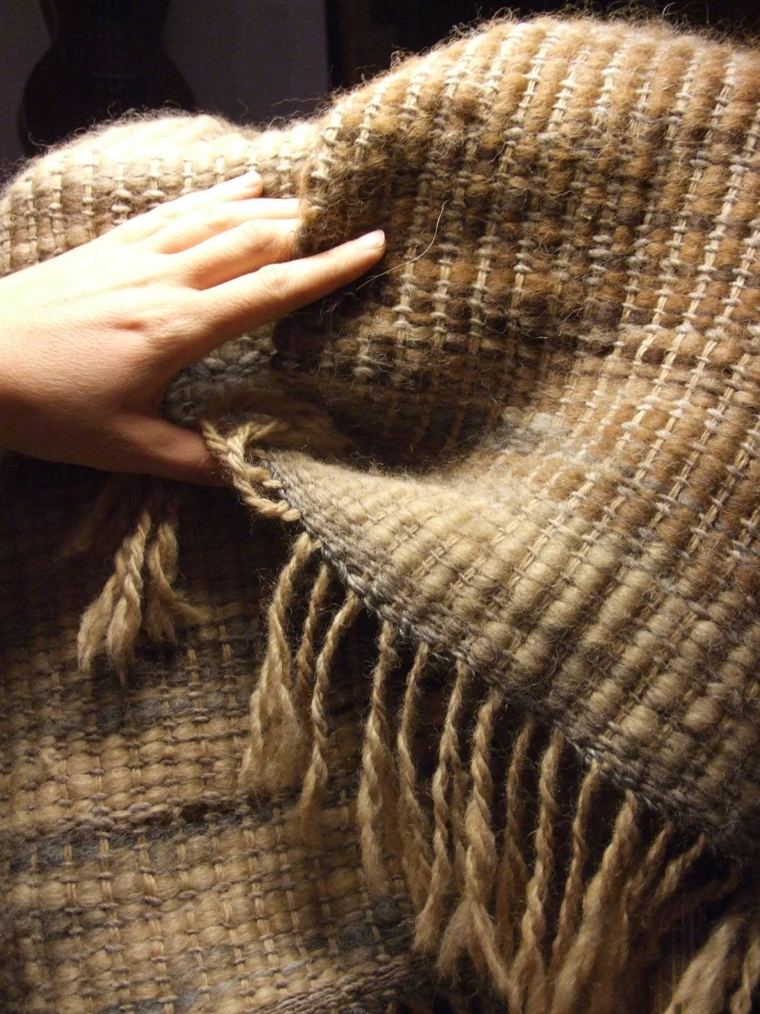 A hand touching a brown and beige woven, fringed textile or blanket. Made at Monte Frio Alpacas. 