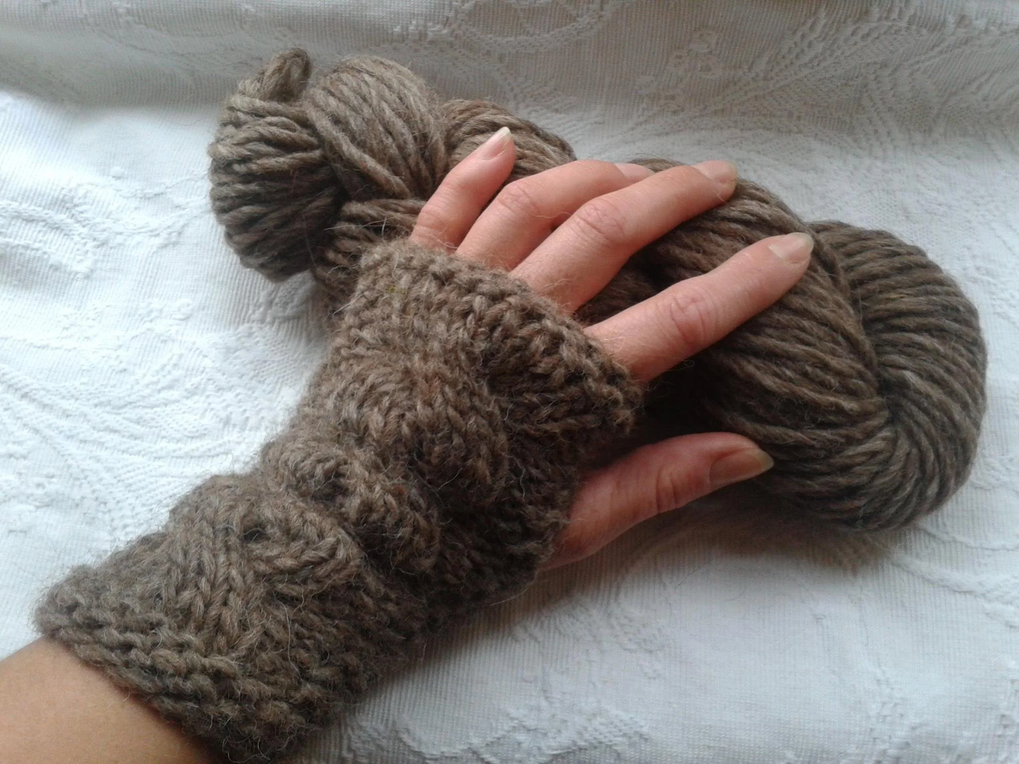 A hand wearing hand knitted gloves, holding a thick, braided, brown wool. Made at Monte Frio Alpacas. 