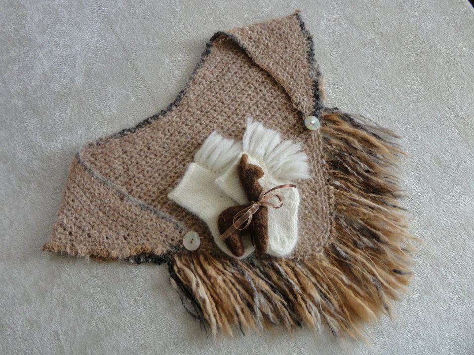 A beige shawl with fringes, two white socks, and a small plush teddy bear tied with a ribbon, all laid on a light-colored surface. Made at Monte Frio Alpacas. 