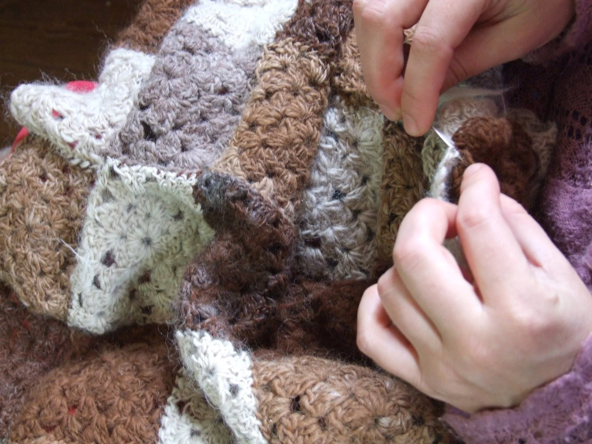 Close-up of hands crocheting a blanket with large, chunky yarn in various shades of brown, cream, and gray. Made at Monte Frio Alpacas.