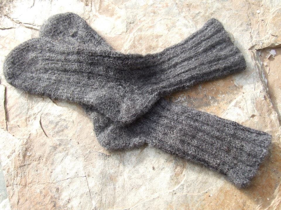 A pair of gray wool socks with a ribbed pattern, placed on a cream blanket of wool. Made at Monte Frio Alpacas.