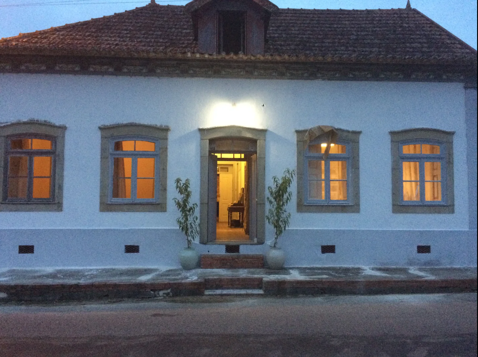 Monte Frio Alpacas house at dusk with a lit interior. The house has a tiled roof, four windows with warm yellow lights.