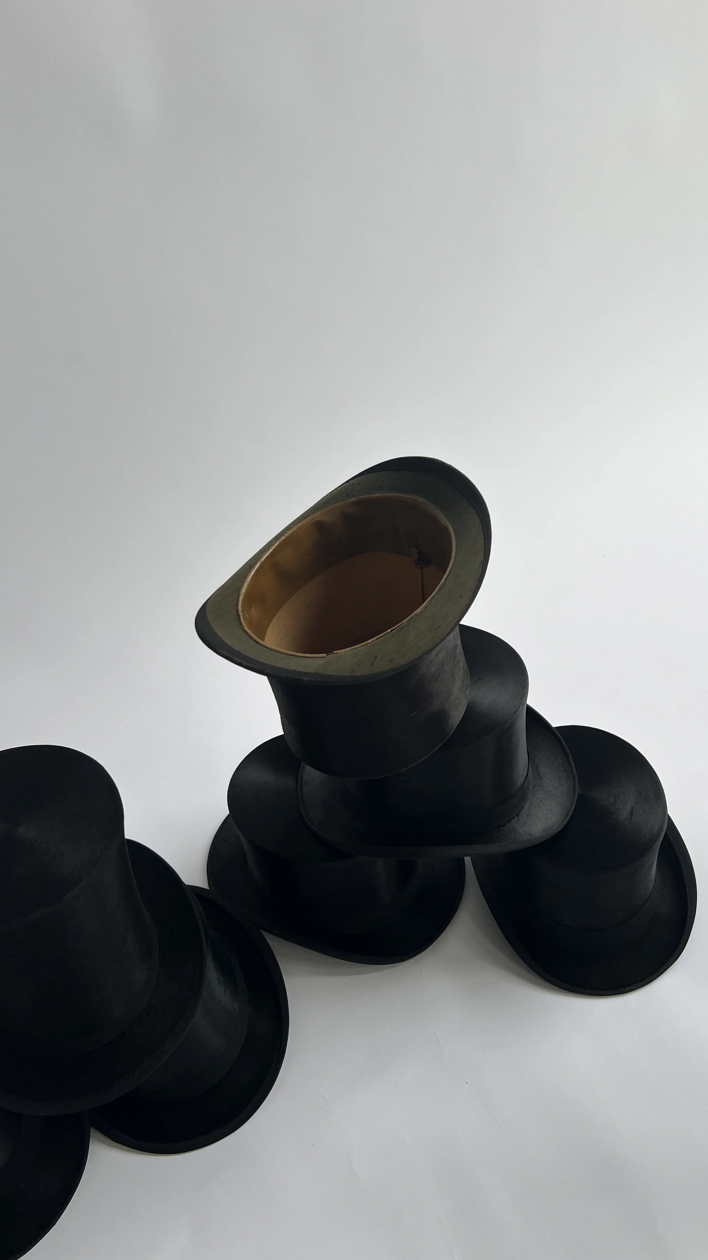 Close-up photograph of several silk top hats, in an elegant pile.