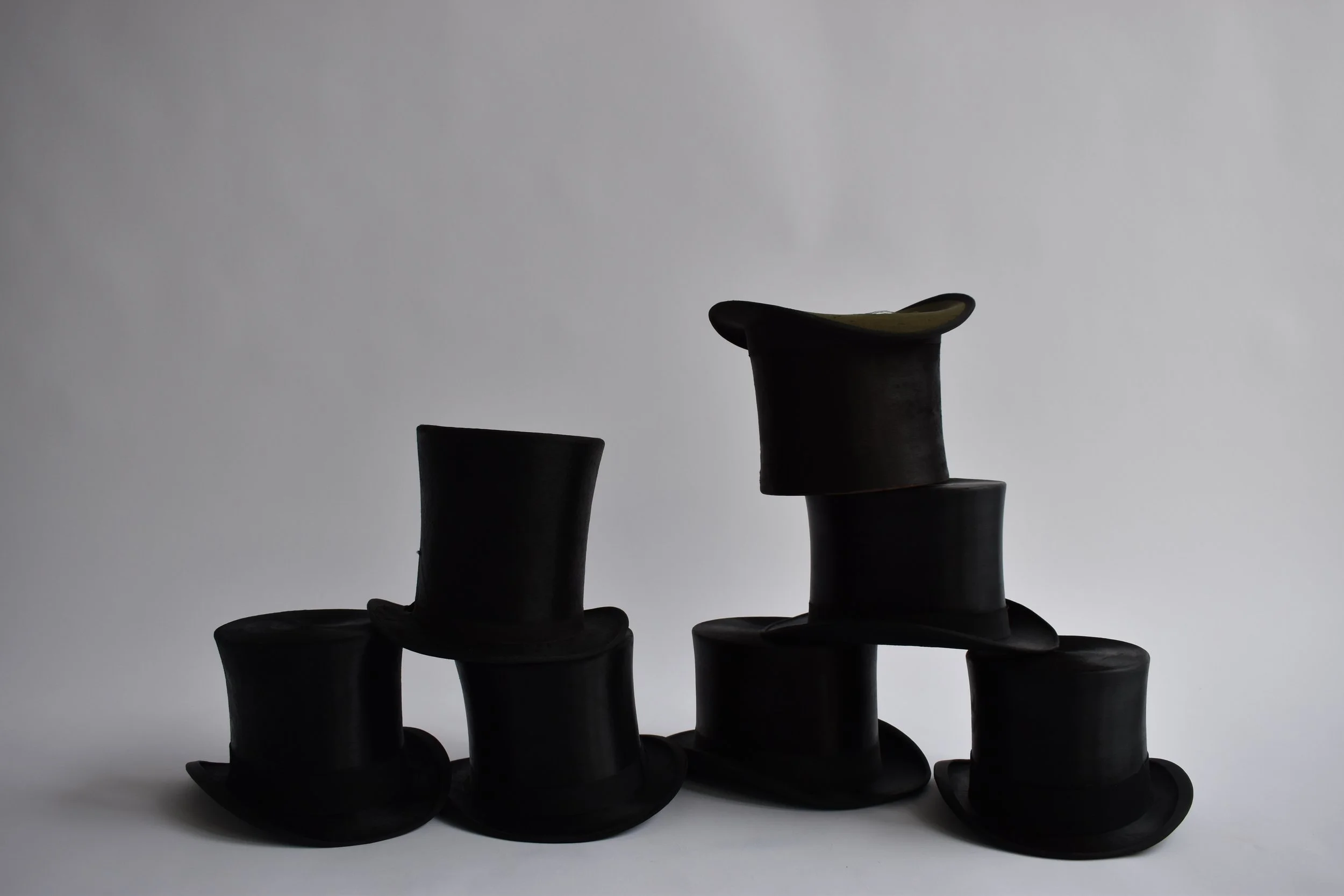 Several black top hats arranged in a row with one hat on top of another, against a plain light background.