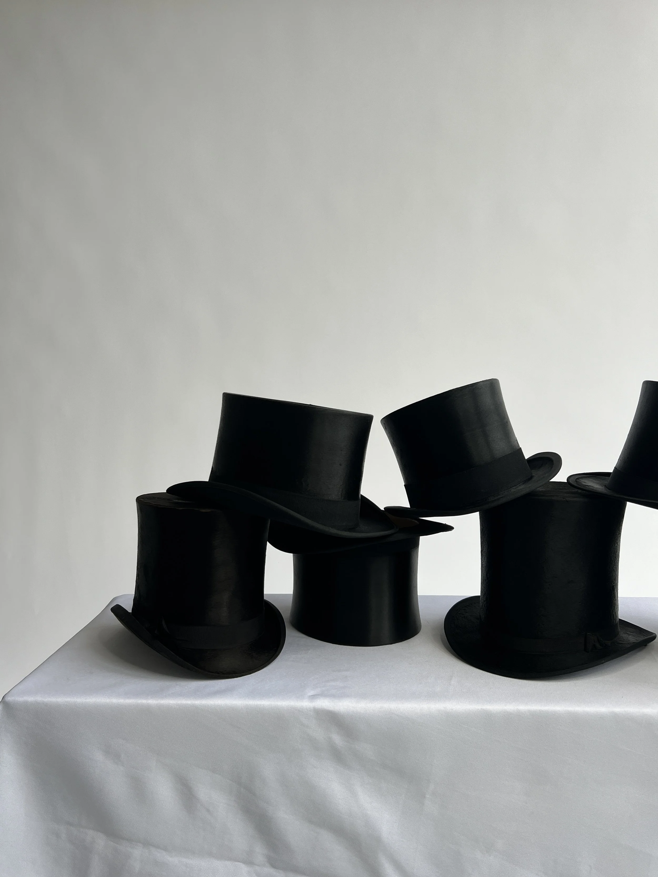 A group of black top hats arranged on a white table against a plain white background.