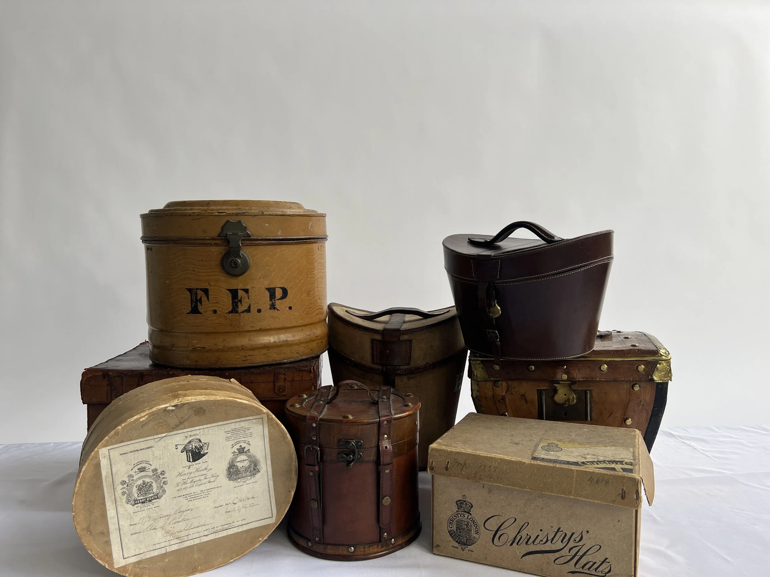Collection of vintage suitcases, hats, and framed documents displayed on a surface against a plain background.